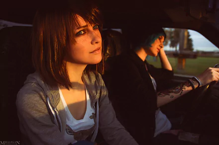 HD desktop wallpaper featuring women cosplaying Max Caulfield and Chloe Price from Life Is Strange, sitting in a car with sunlight casting a warm glow.