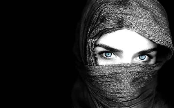 A striking HD desktop wallpaper featuring a woman with captivating blue eyes, partially concealed by a dark scarf against a black background.