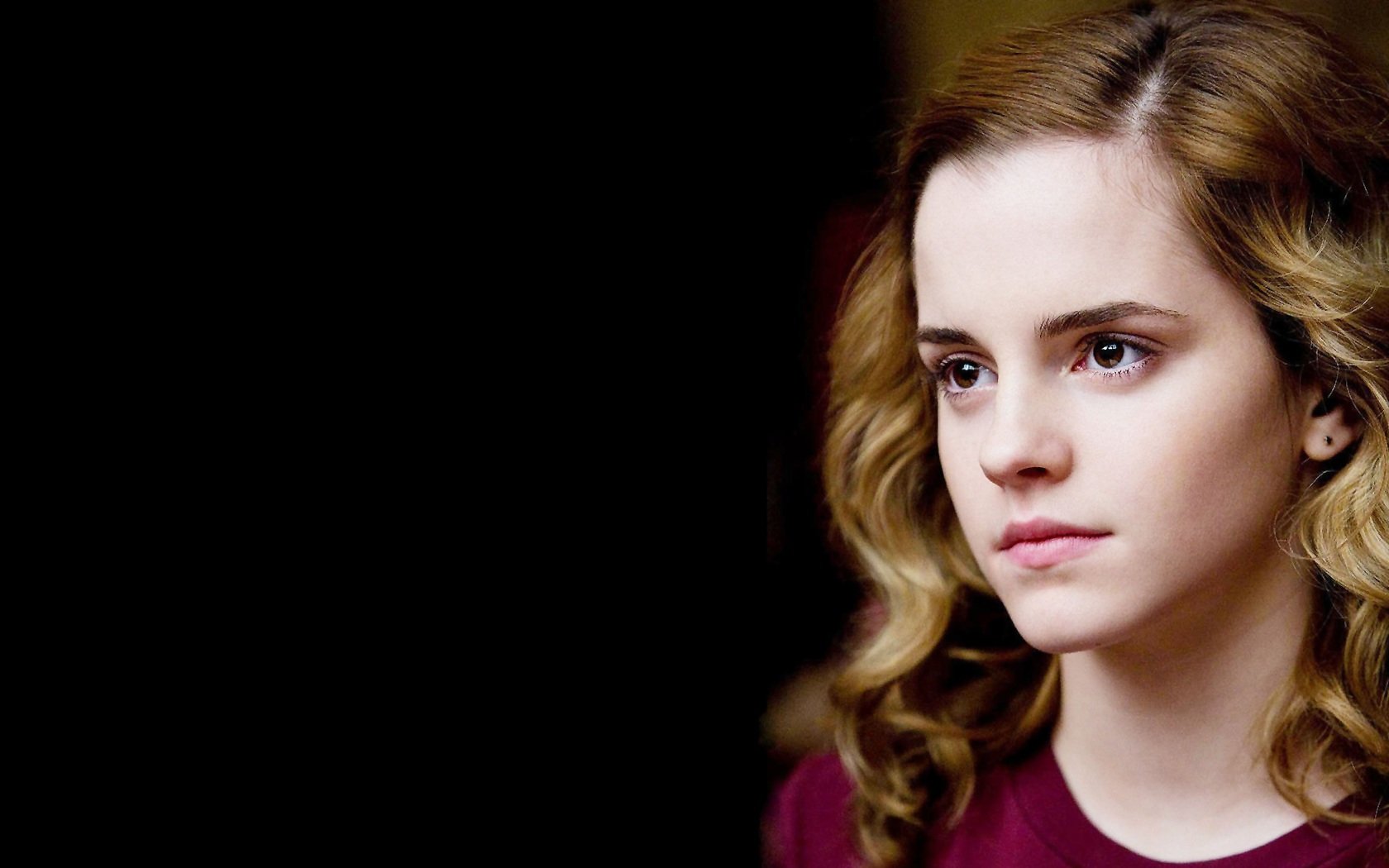 HD desktop wallpaper of celebrity Emma Watson, featuring a close-up portrait with a slight smile and wavy hair, set against a dark background.
