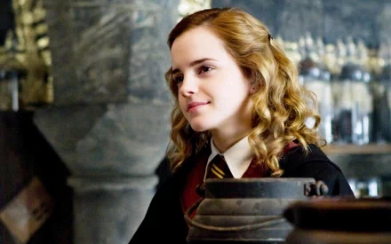 Hermione Granger (Emma Watson) in Harry Potter and the Half-Blood Prince, depicted in a HD desktop wallpaper and background. She is shown smiling in a classroom setting within Hogwarts.
