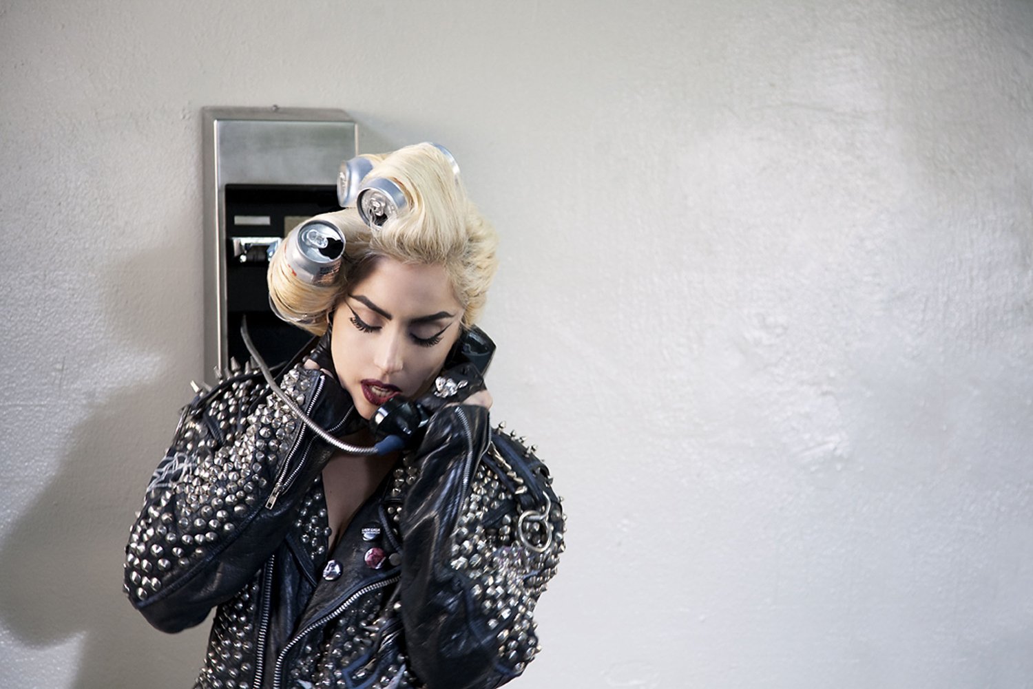 HD PC desktop wallpaper featuring Lady Gaga in a studded black leather jacket, speaking on a wall-mounted payphone, blending music and edgy style.