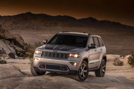 Silver Jeep Grand Cherokee SUV parked on rocky terrain with mountains in the background, featured as an HD PC desktop wallpaper and background.