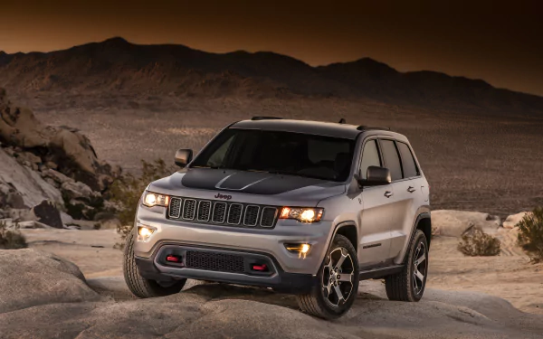 Silver Jeep Grand Cherokee SUV parked on rocky terrain with mountains in the background, featured as an HD PC desktop wallpaper and background.