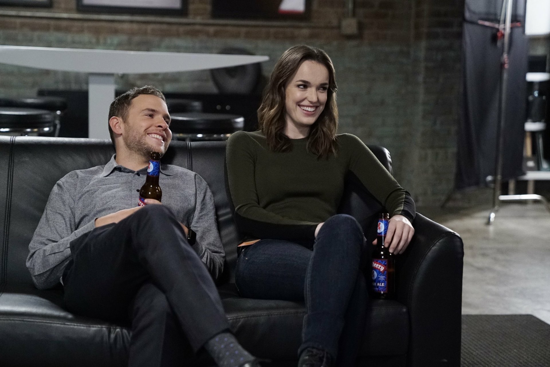 Iain De Caestecker and Elizabeth Henstridge from the TV show Agents of S.H.I.E.L.D. sit and smile on a black leather couch in this HD PC desktop wallpaper.