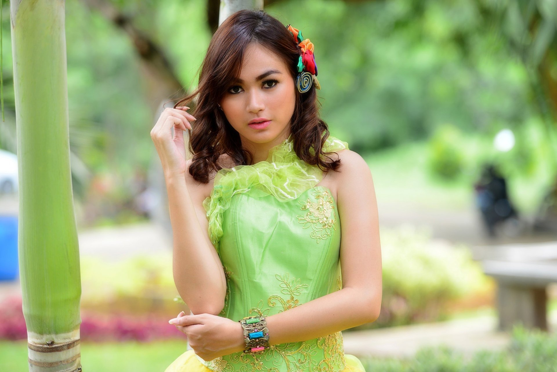 HD PC desktop wallpaper of a brunette model in a green dress, brown-eyed woman posed outdoors with soft shallow depth of field and a lush blurred background.
