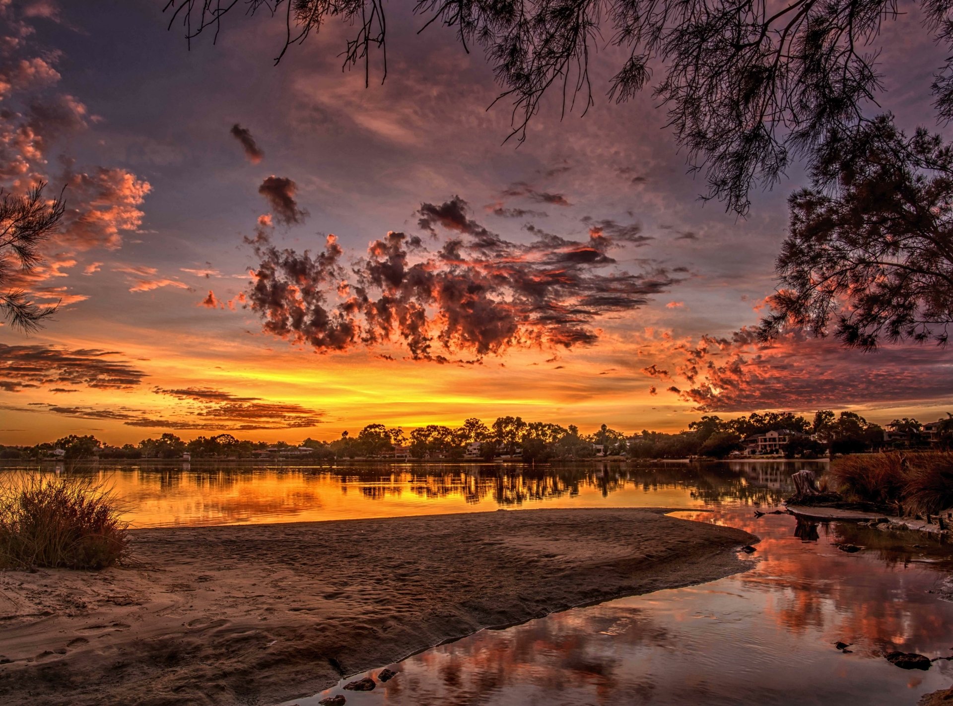 A vibrant sunset over Swan River at Salter Point, Western Australia, with dramatic clouds reflecting on the calm water, surrounded by natural landscape.
