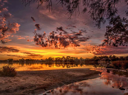 A vibrant sunset over Swan River at Salter Point, Western Australia, with dramatic clouds reflecting on the calm water, surrounded by natural landscape.
