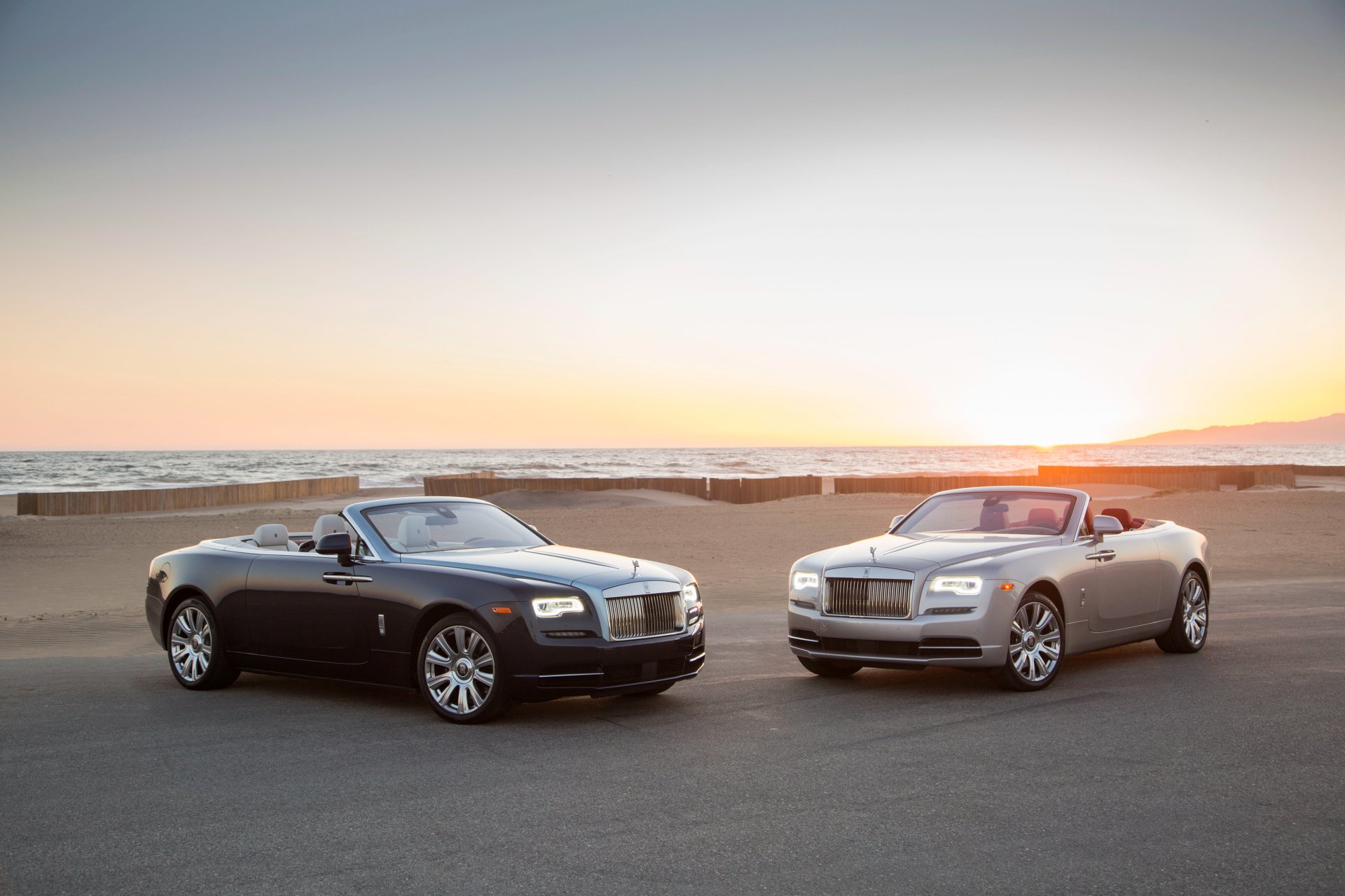 Two Rolls-Royce Dawn grand tourers, silver and black, parked by the coast at sunset. 4K Ultra HD PC desktop wallpaper background.