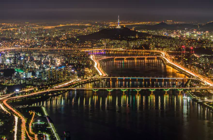 A stunning HD wallpaper of Seoul's night cityscape featuring illuminated bridges over a river, with the city lights creating a vibrant glow against the dark sky in South Korea.