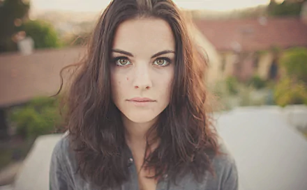 HD desktop wallpaper featuring a close-up of American actress Jaimie Alexander with hazel eyes and loose dark hair against a blurred outdoor background.
