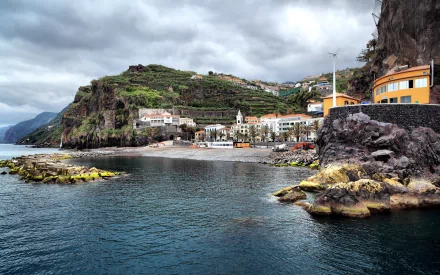A coastal view of Ponta Do Sol in Portugal, showcasing a charming village nestled between lush hills and the ocean, highlighted by rocky shores and a serene waterfront.