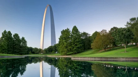 The Gateway Arch stands majestically over a serene pond, surrounded by lush greenery, embodying St. Louis's iconic man-made monument in stunning HD quality.