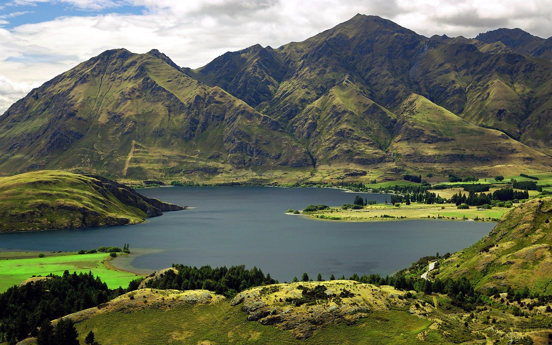 A stunning HD wallpaper showcasing a serene lake surrounded by lush green hills and majestic mountains, capturing the beauty of nature in a breathtaking landscape.