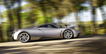 A stunning HD wallpaper of a silver Pagani Huayra supercar speeding on a road, set against a blurred background of lush green trees.