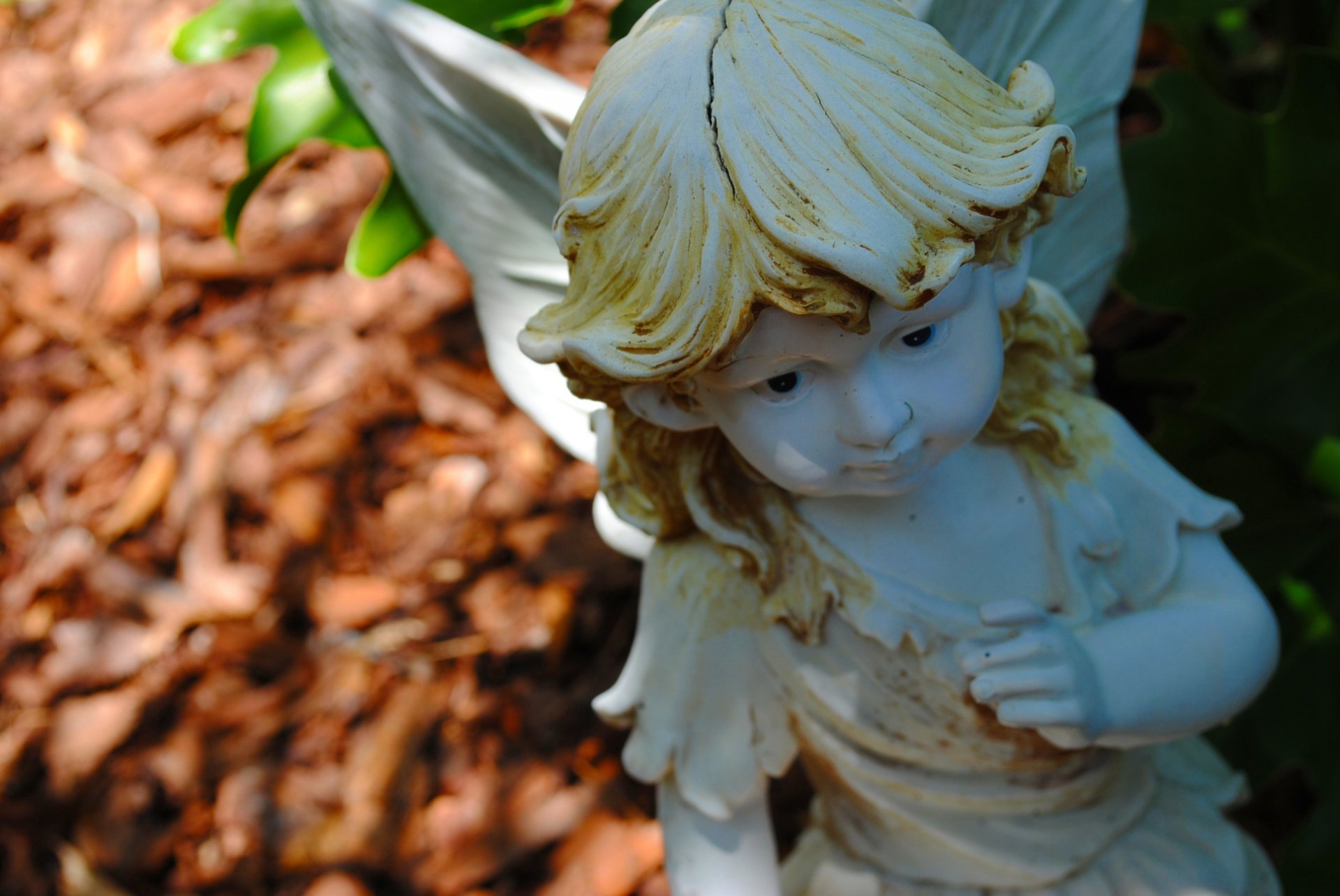 HD desktop wallpaper featuring a close-up of a man-made statue of a young angel with blond hair, set against a blurred natural background.