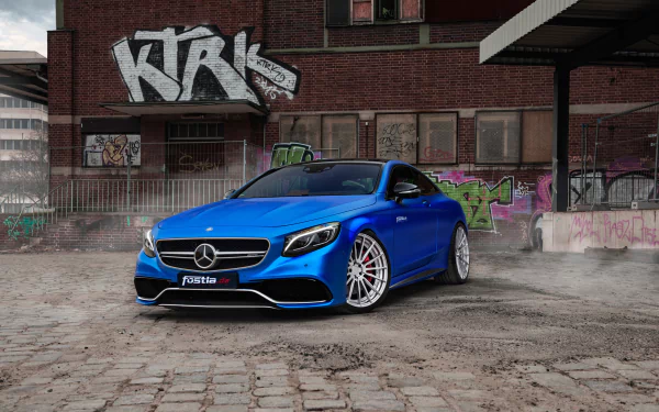 Blue Mercedes-Benz S63 AMG parked on a cobblestone street in front of an urban building with graffiti, featured as an HD PC desktop wallpaper and background.