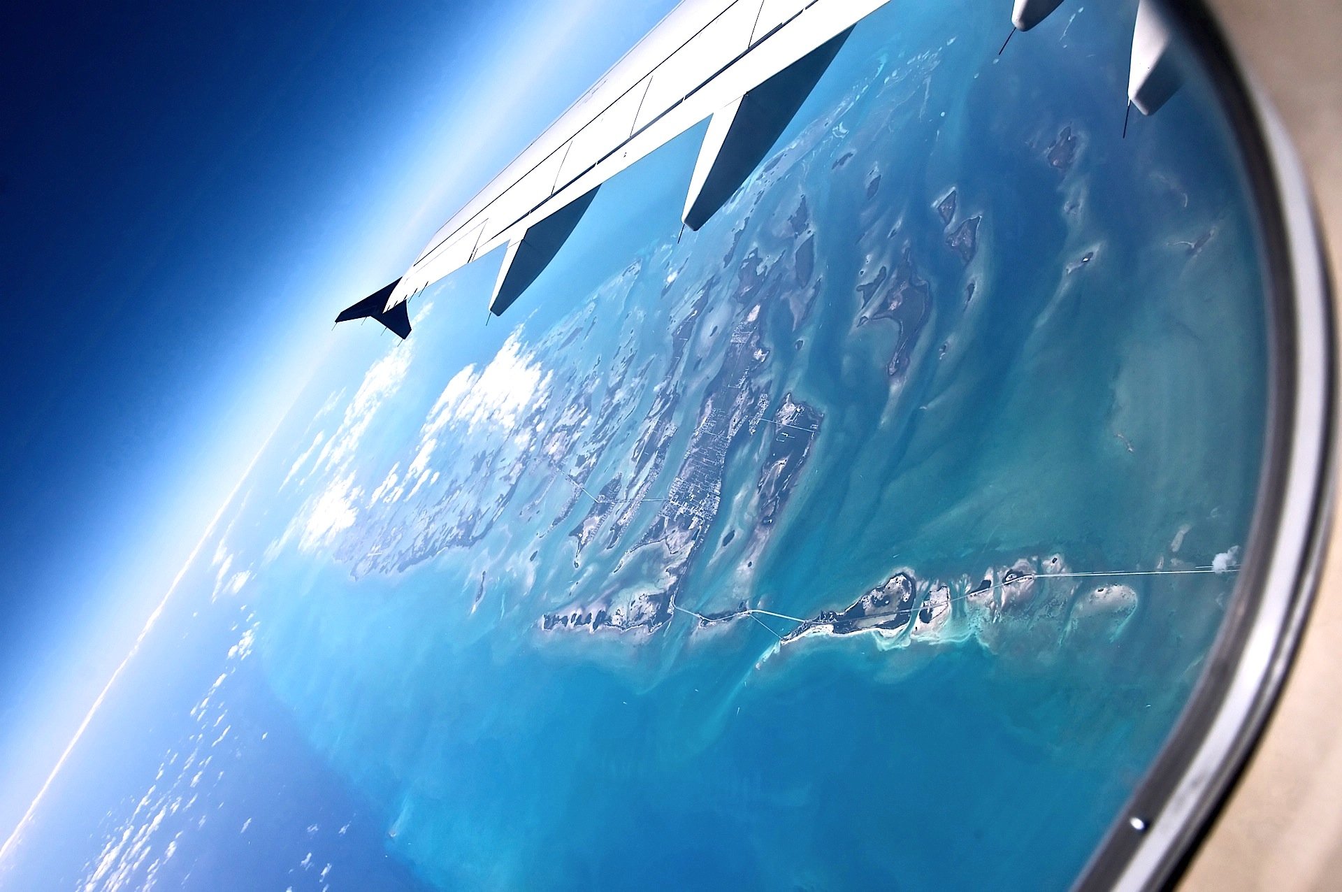 Aerial view of an island surrounded by ocean water, seen through an airplane window, showcasing nature from above in this HD desktop wallpaper.