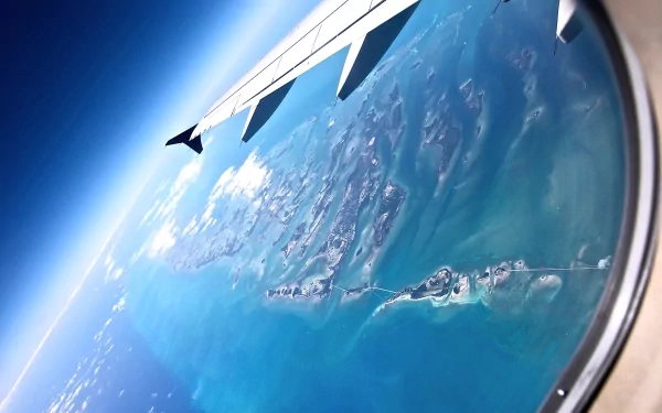 Aerial view of an island surrounded by ocean water, seen through an airplane window, showcasing nature from above in this HD desktop wallpaper.