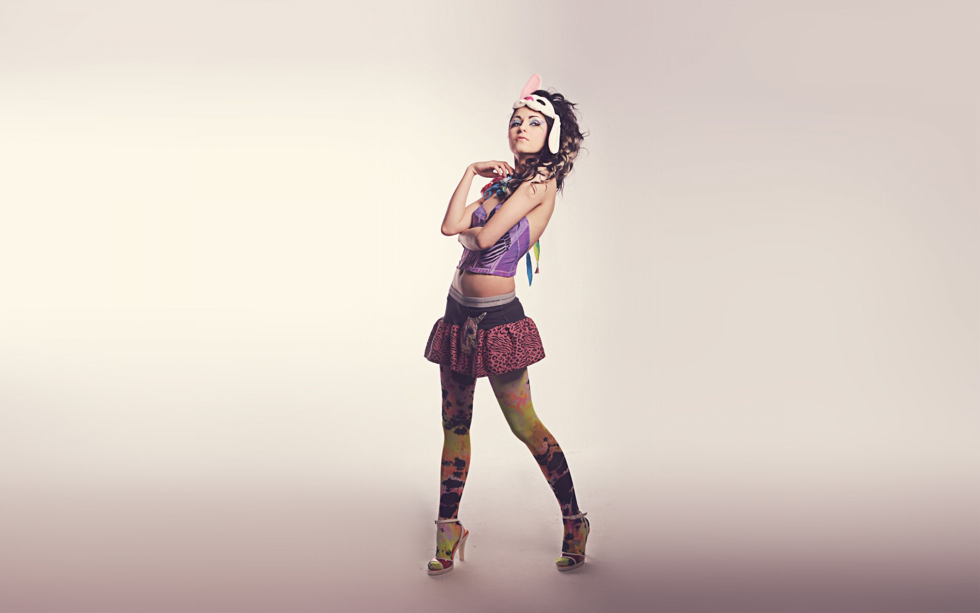 HD desktop wallpaper of a stylish woman posing confidently in colorful clothing and high heels against a minimalist, light background.