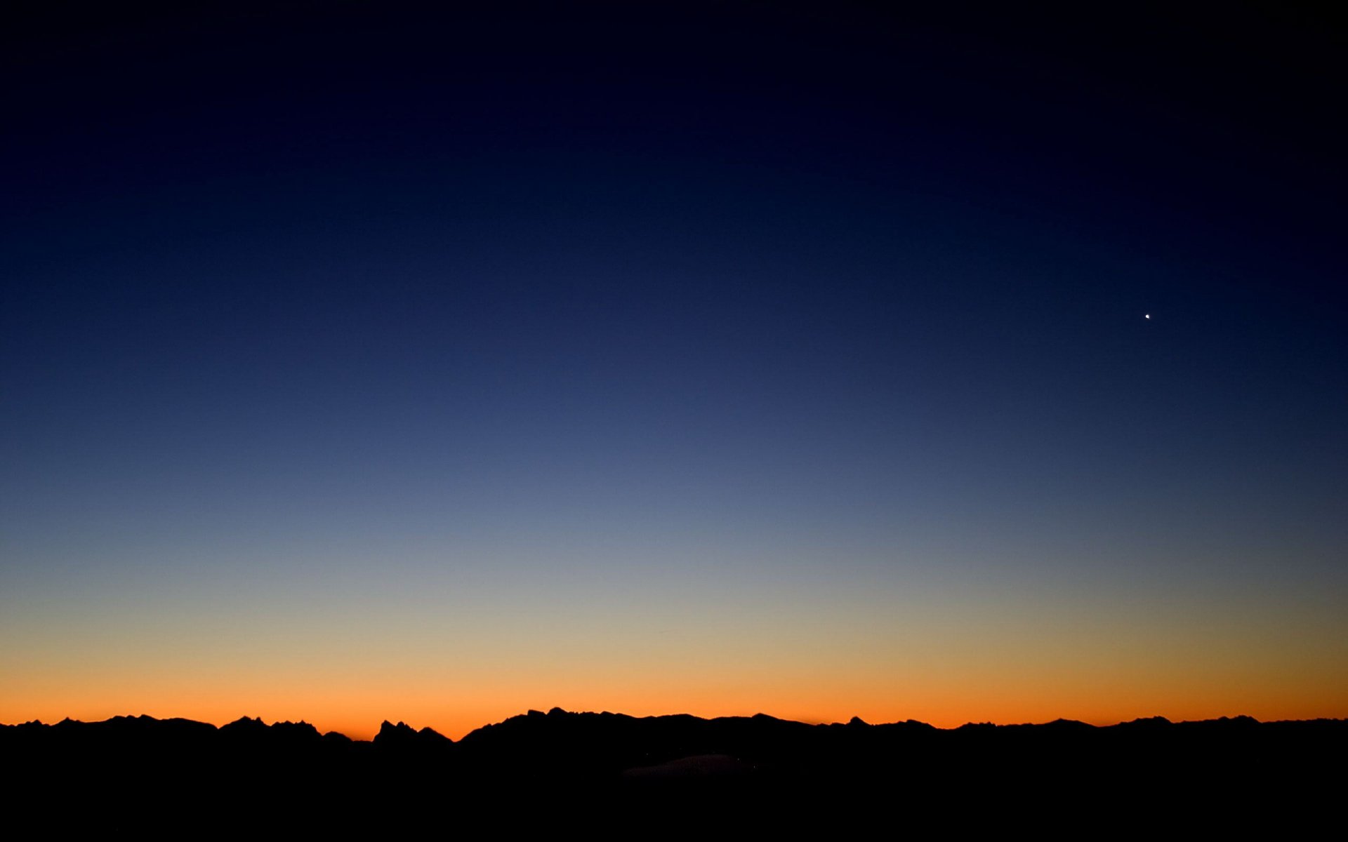 A stunning HD wallpaper capturing a serene sunrise over silhouetted mountains, blending rich hues of blue and orange, showcasing the beauty of nature.