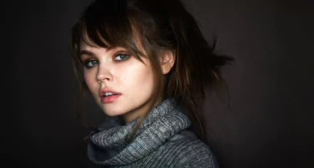 An HD desktop wallpaper featuring a brunette Russian model, Anastasiya Scheglova, with a soft expression and tousled hair against a dark background, wearing a gray turtleneck sweater.