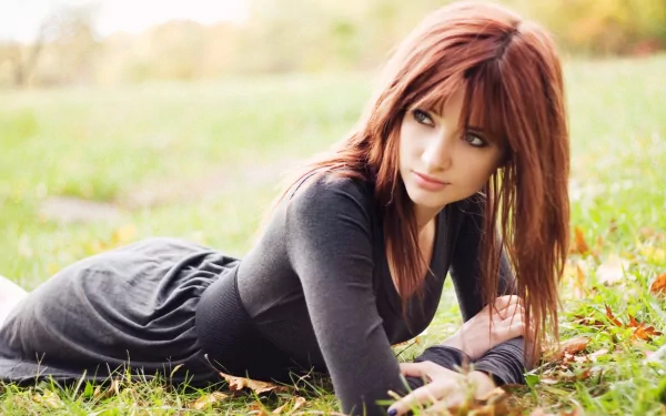 A high-definition desktop wallpaper featuring Susan Coffey, captured in a serene outdoor setting, lying on the grass with autumn foliage around her.