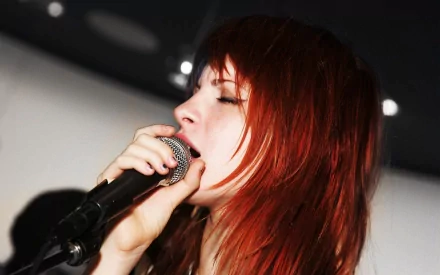 Close-up HD wallpaper of Hayley Williams passionately singing into a microphone, capturing the vibrant energy of Paramore’s music scene.