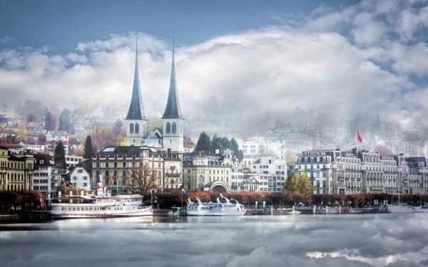 A serene fall scene in Lucerne, Switzerland, featuring historic buildings, twin church spires, boats on the water, and vivid reflections under a cloudy sky.