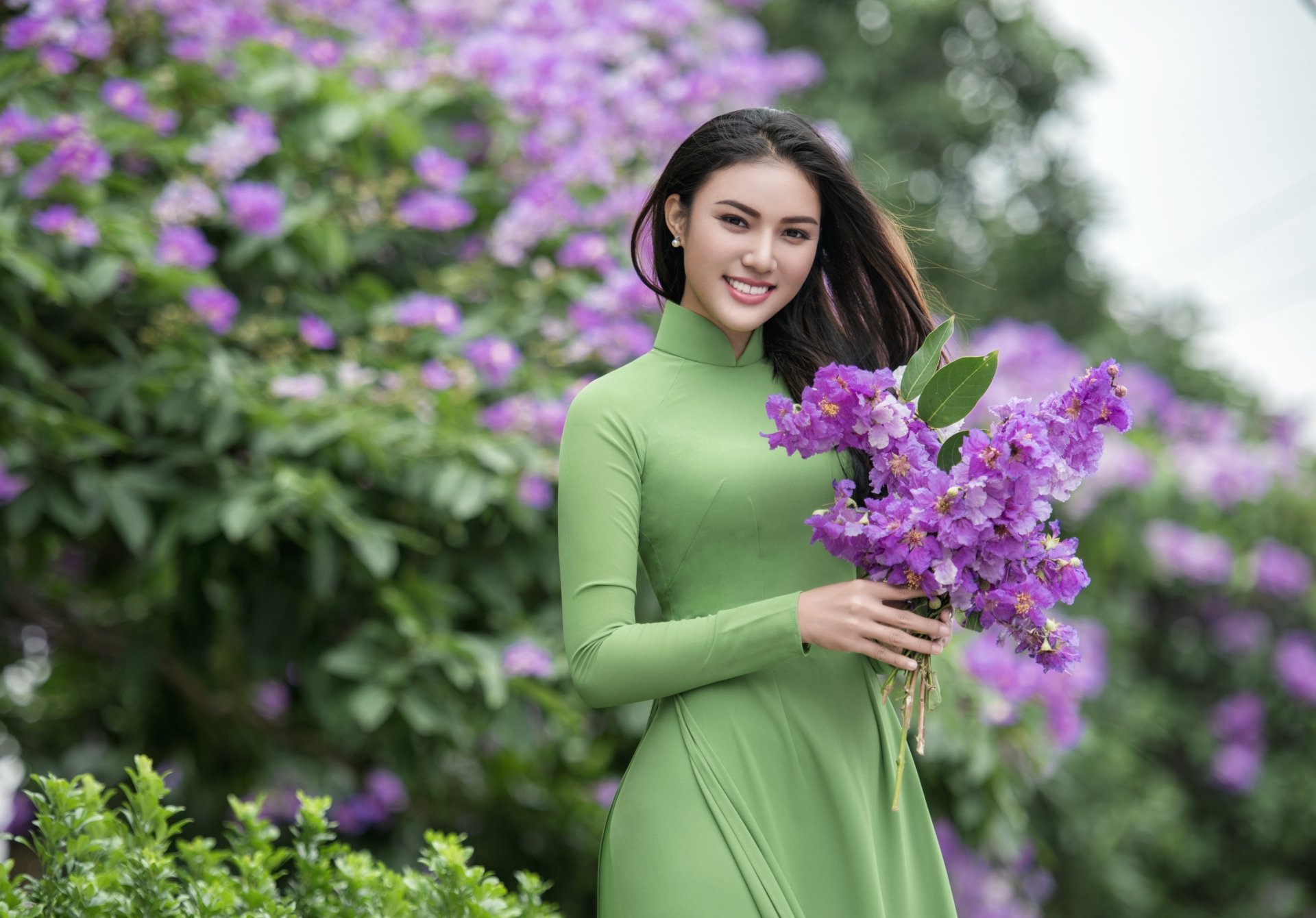 Download Brown Eyes Brunette Smile Depth Of Field Purple Flower Flower Green Dress Model Woman Asian 4k Ultra HD Wallpaper