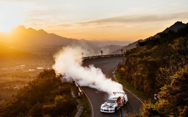 Rally car kicking up smoke on a winding mountain road at sunset — sports rallying action, HD PC desktop wallpaper/background.