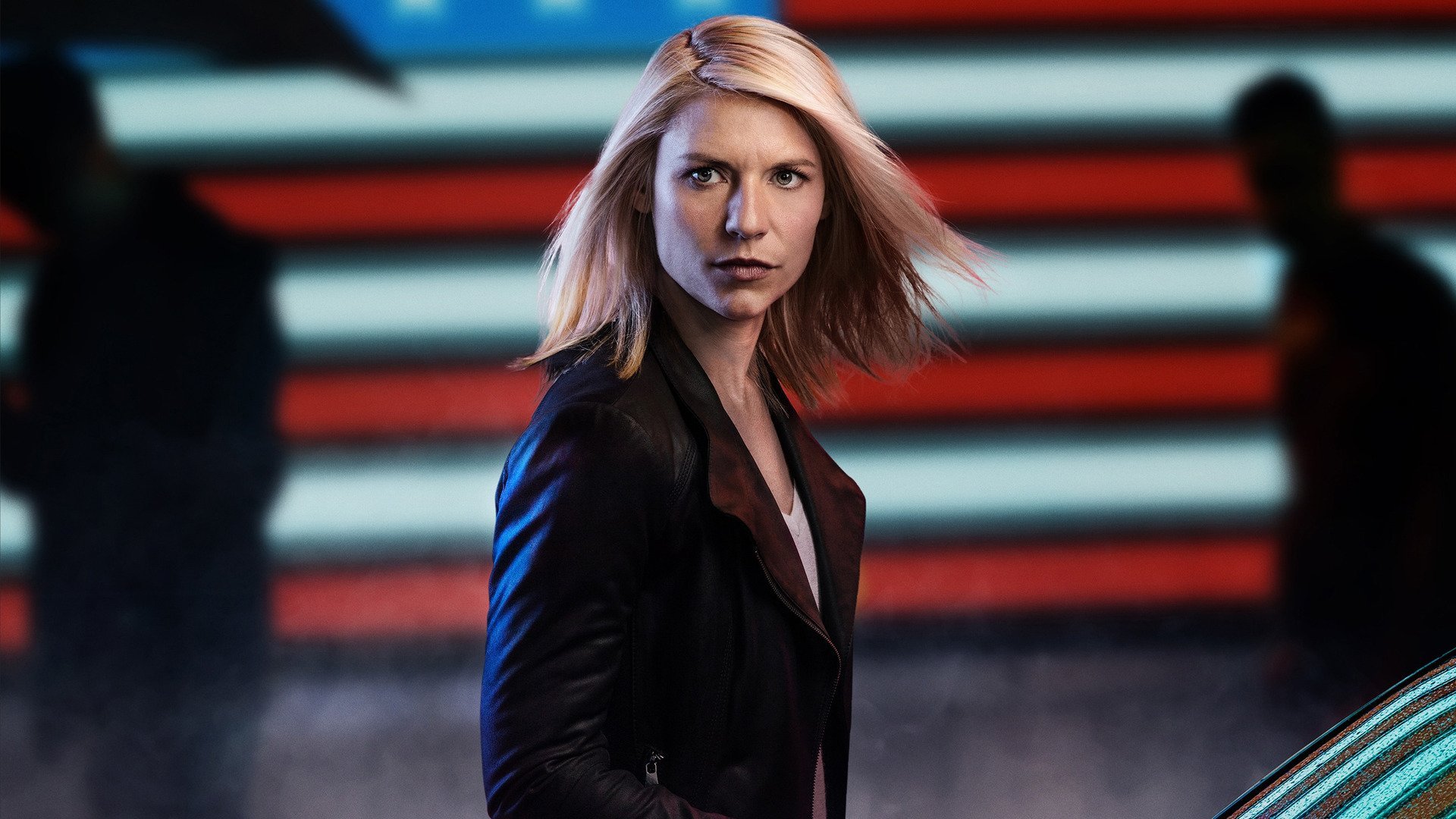 HD PC desktop wallpaper of a determined blonde actress in a dark coat, standing before blurred red, white and blue stripes with a tense, cinematic TV-drama vibe.