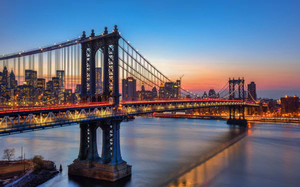 HD PC desktop wallpaper: Manhattan Bridge at sunset in New York, USA — man-made steel spans and city lights reflecting on the East River beneath a vivid sky.