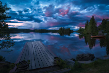 HD desktop wallpaper features a serene Norwegian lake at sunset, with a wooden pier extending into calm, reflective waters. Dramatic clouds and vibrant colors enhance the tranquil landscape photography.
