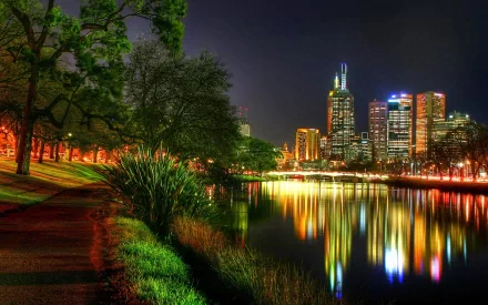 Night view of Melbourne city skyline lighting up the Yarra River, Australia, with vibrant reflections and lush greenery along the riverbank.