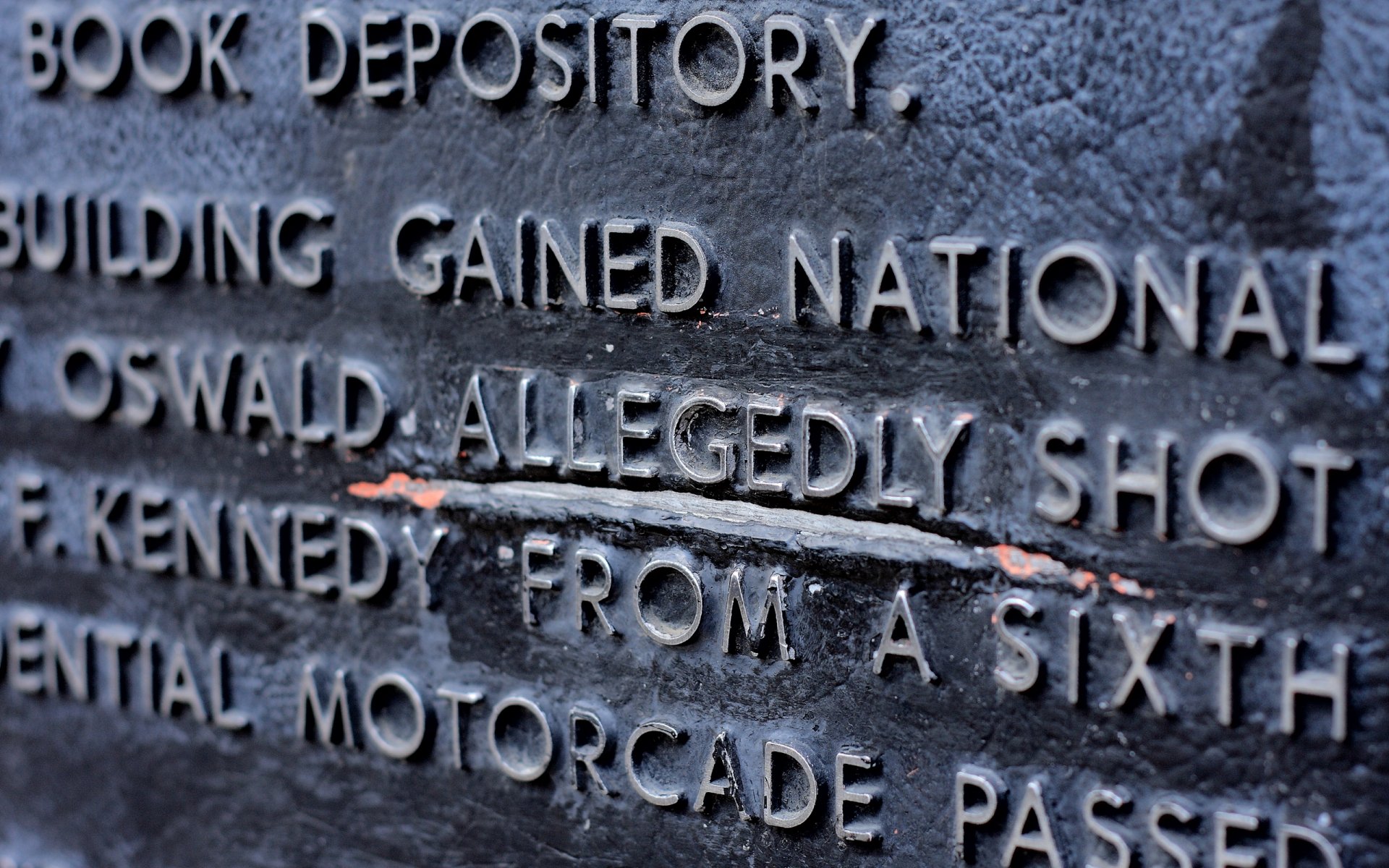 Close-up of a historical plaque detailing the site of the Book Depository, with inscriptions about Oswald and the events surrounding JFK's assassination. HD desktop wallpaper background.