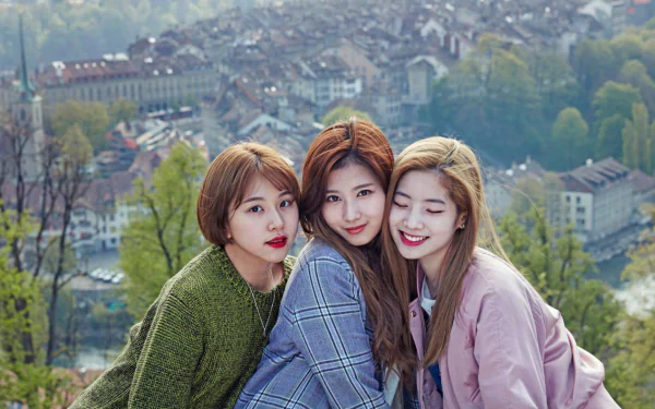 Three members of the music group TWICE pose together outdoors with a scenic background of a town. This HD desktop wallpaper and background captures their close bond.
