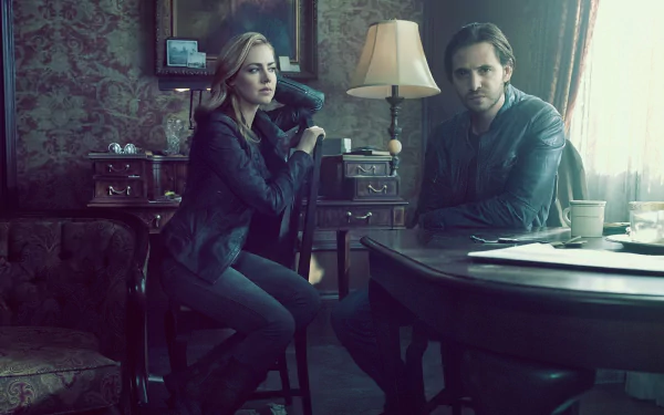 Two characters from the TV show 12 Monkeys sit at a dim vintage parlor table under a lamp, moody teal tones. HD PC desktop wallpaper and background.