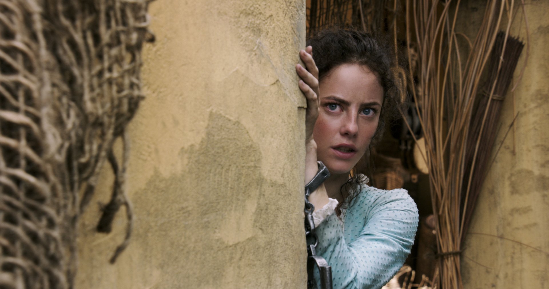 Carina Smyth, played by Kaya Scodelario, peeks cautiously from behind a weathered wall in a scene from the movie Pirates of the Caribbean: Dead Men Tell No Tales.