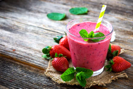 A vibrant strawberry smoothie in a glass garnished with mint leaves and a striped straw, surrounded by fresh strawberries on rustic wooden surface, captured in 4K Ultra HD.