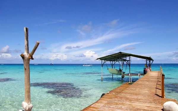 A serene beach scene featuring a wooden pier extending over clear blue waters, under a sky filled with clouds, creating a tranquil atmosphere at a picturesque coastline.