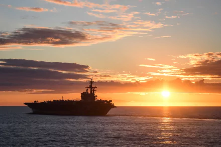 The USS George H.W. Bush (CVN-77) aircraft carrier sails at sunset on the horizon, creating a striking military-themed HD desktop wallpaper.