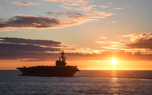 The USS George H.W. Bush (CVN-77) aircraft carrier sails at sunset on the horizon, creating a striking military-themed HD desktop wallpaper.