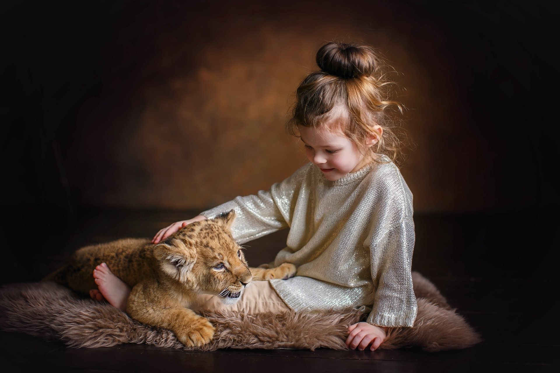 A little girl gently petting a lion cub, captured in a warm, intimate photography setting as an HD desktop wallpaper.
