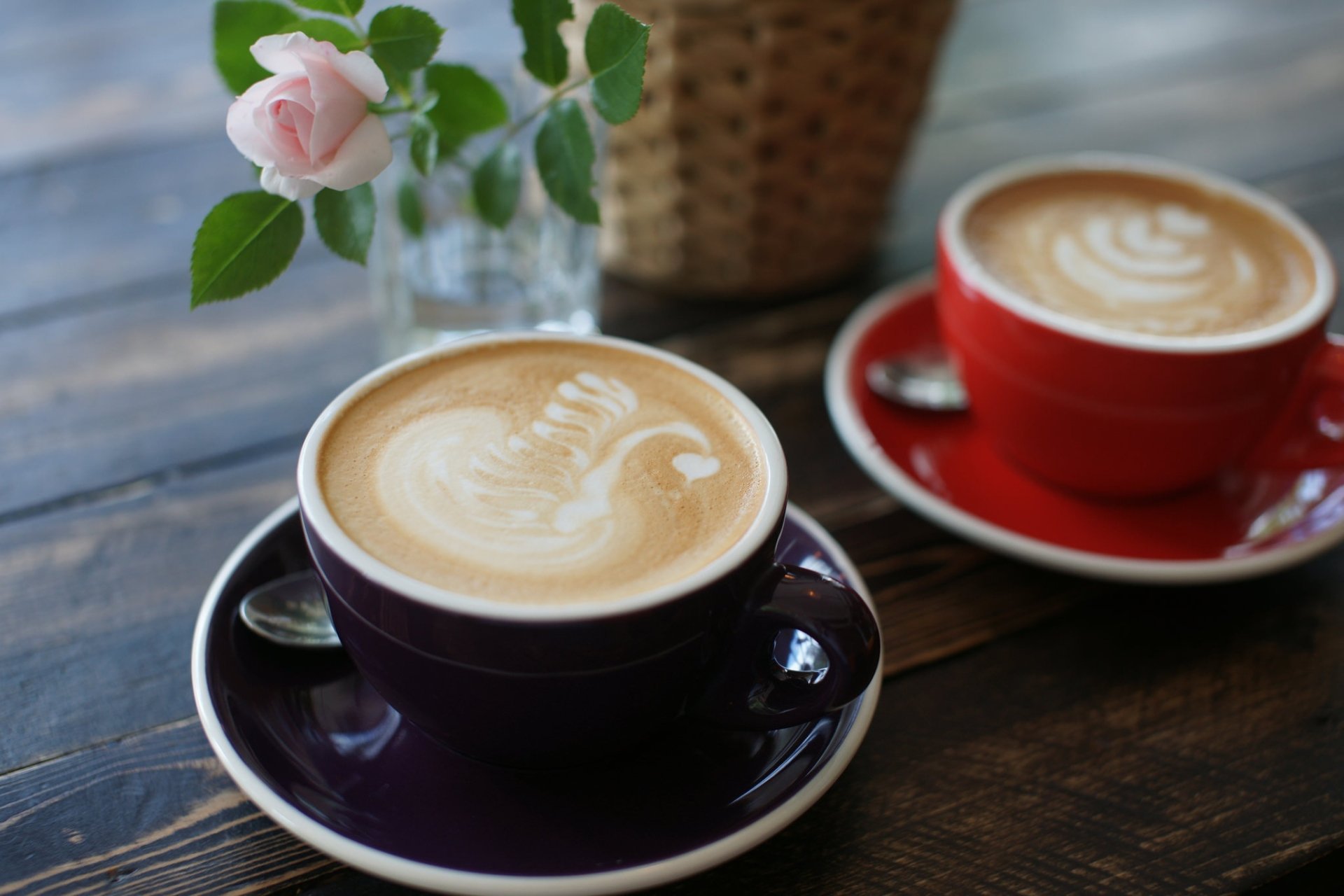 HD desktop wallpaper featuring two cups of coffee with latte art on a wooden table, accompanied by a pink rose in a glass vase.