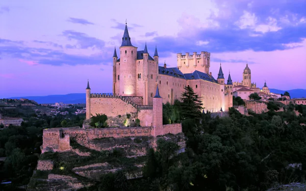 HD desktop wallpaper of Segovia Castle in Spain, showcasing stunning architecture against a vibrant twilight sky in a picturesque landscape.