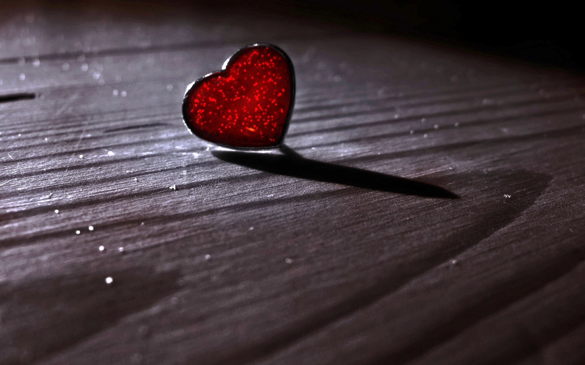 A close-up of a sparkling red heart resting on wooden planks, casting a soft shadow, beautifully capturing the theme of love in this artistic HD wallpaper.