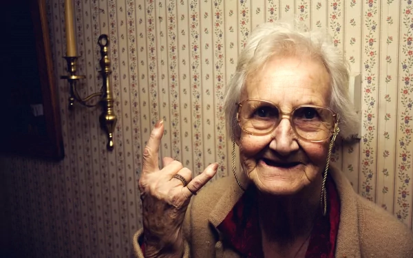 A humorous HD desktop wallpaper featuring an elderly woman flashing a rock sign, smiling widely against a patterned wall, capturing a joyful and playful spirit.