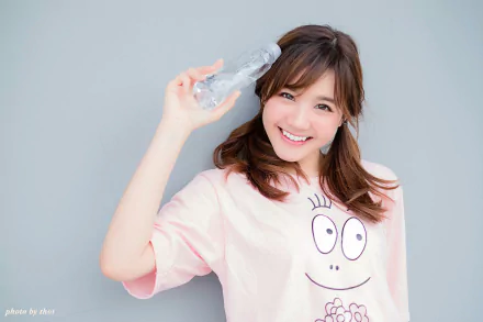 HD desktop wallpaper featuring an Asian woman smiling, holding a water bottle, and wearing a pink shirt with a cute face design against a light gray background.