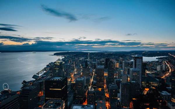 A stunning HD cityscape of Seattle, USA at dusk, featuring skyscrapers against a vibrant horizon over water, capturing the man-made urban skyline.