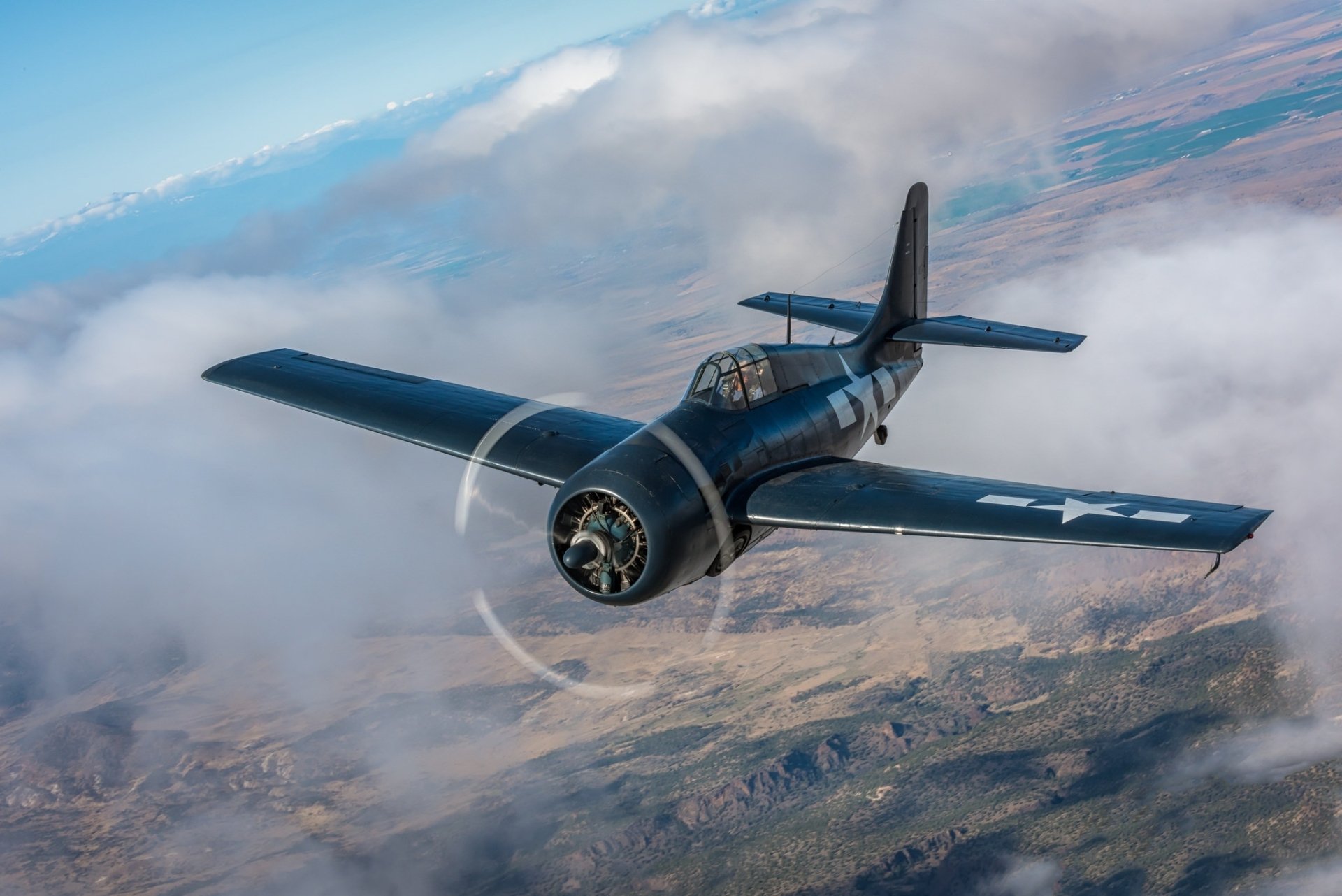 HD desktop wallpaper featuring a Grumman F4F Wildcat warplane soaring above clouds, showcasing the iconic military aircraft in flight.